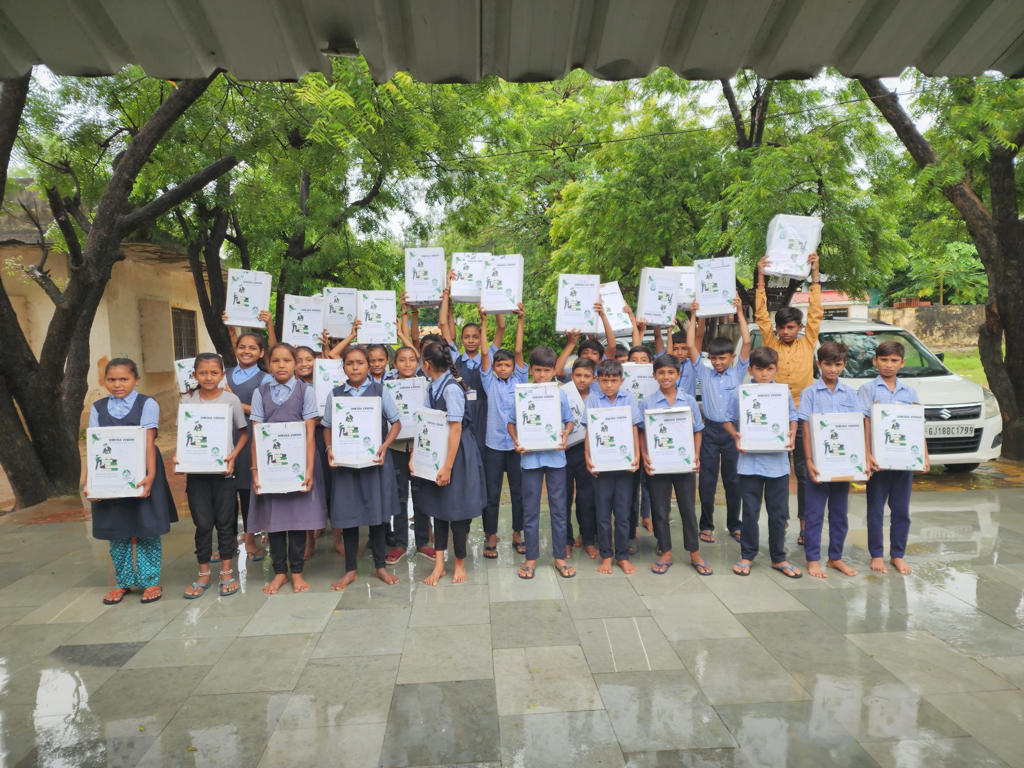 Students holding up educational kits outside under trees